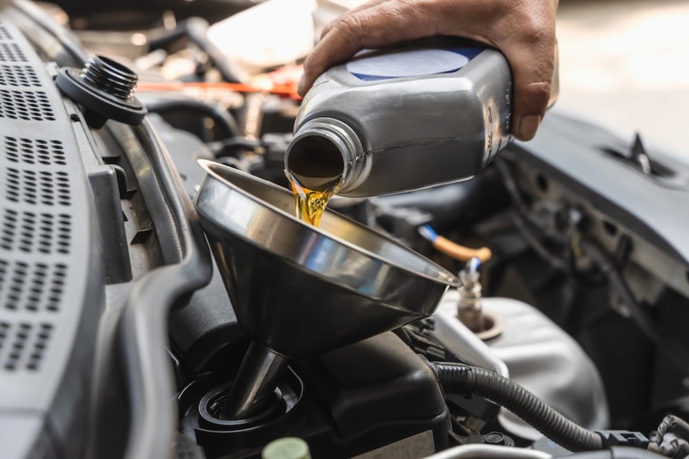 A service technician pouring engine oil into a vehicle’s engine