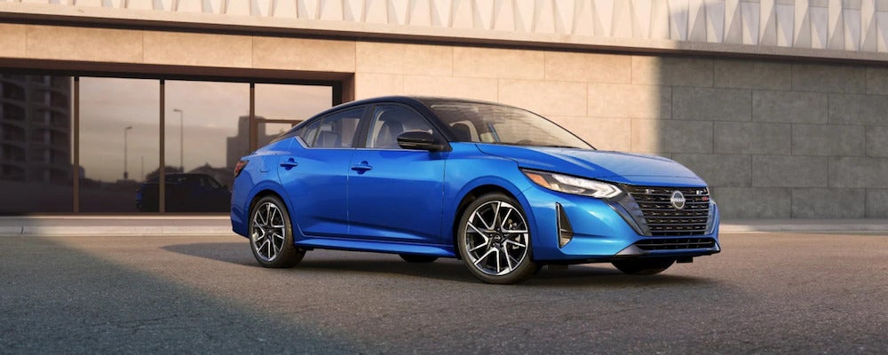 A three-quarters view of a bright blue 2025 Nissan Sentra sedan parked in front of a stone building
