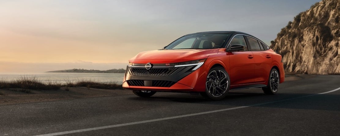 A red 2026 Nissan Sentra sedan driving down a seaside road at sunset