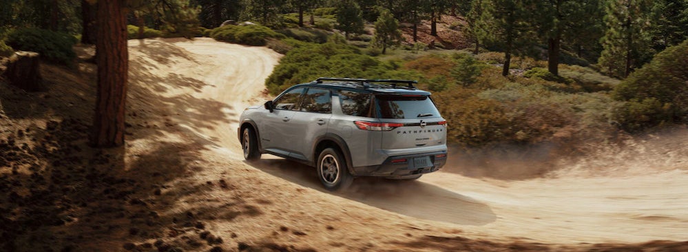 A white 2026 Nissan Pathfinder SUV driving over a dusty dirt trail through woodland