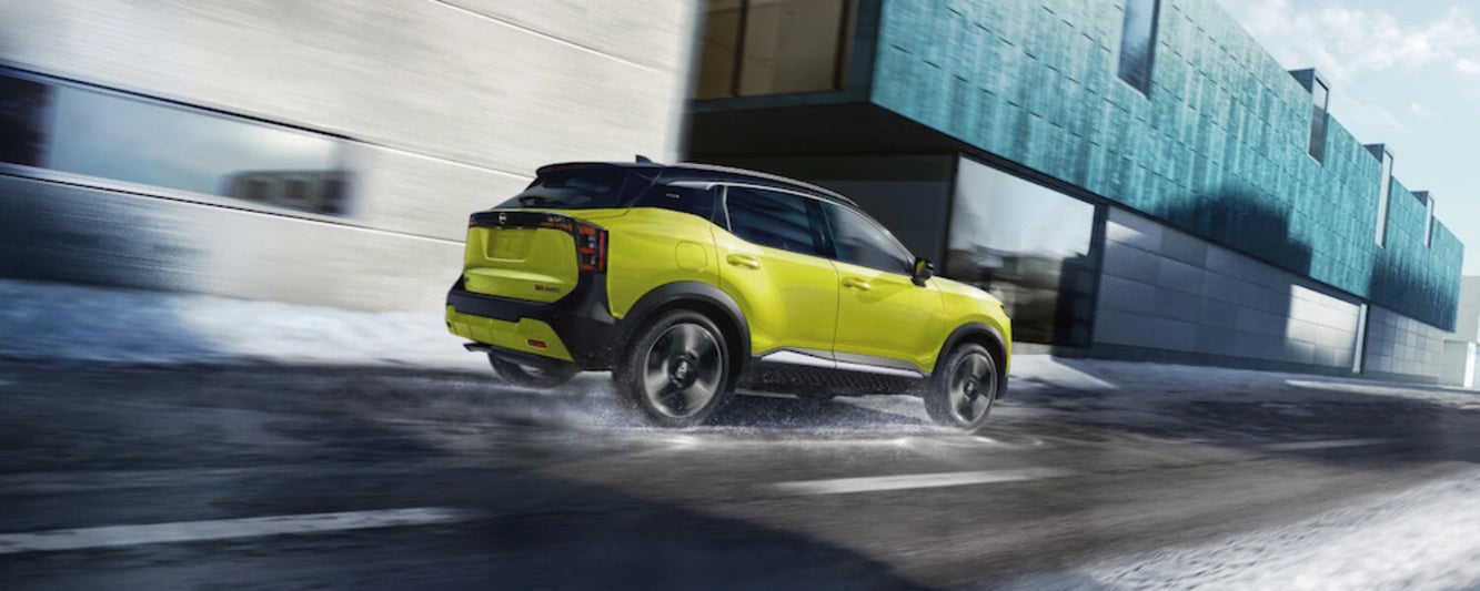 A chartreuse 2026 Nissan Kicks SUV driving down a rainy city street