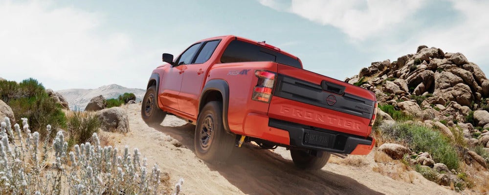 An orange 2026 Nissan Frontier pickup truck driving over rocky desert terrain