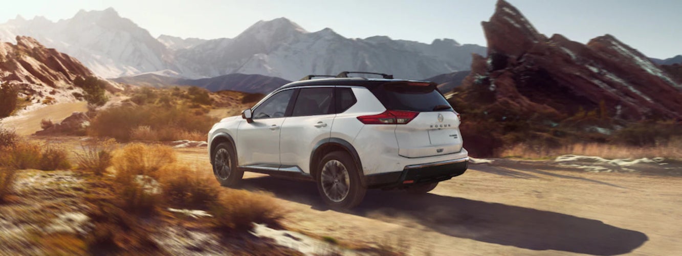 A white 2025 Nissan Rogue SUV driving over dry, rocky terrain
