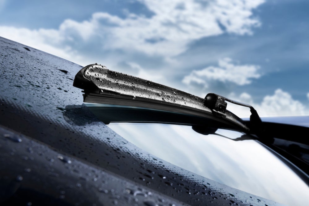 A close up of a windshield wiper on a vehicle’s windshield, with a blue sky and clouds in the background
