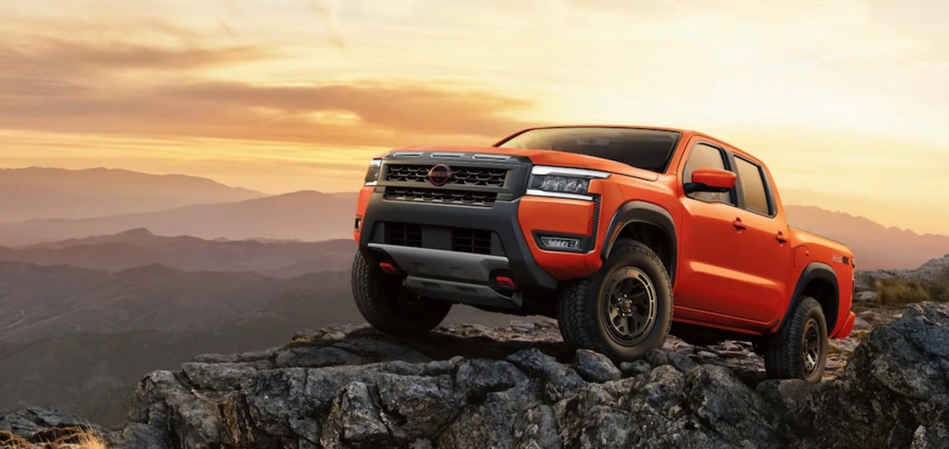 An orange 2026 Nissan Frontier pickup truck parked on a rocky outcropping at sunset